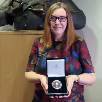 Prof. Sarah Gilbert with her Rosalind Franklin Medal, standing in front of a statue of Edward Jenner at the Jenner Institute.