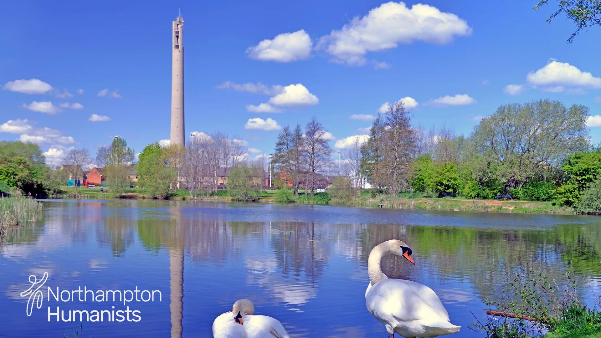 National Lift Tower stands against a bright blue sky, with swans swimming on a body of water in the foreground. The Happy Human logo and 'Northampton Humanists' in white on bottom left of image.