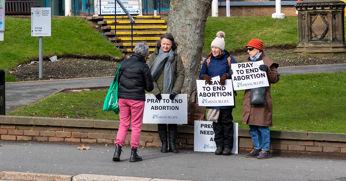 Pro-life protesters outside an abortion clinic, with placards to harass women using the clinic