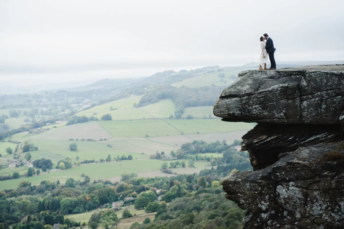 The bride and groom kiss, high up on a rocky outcrop, the dramatic landscape behind them