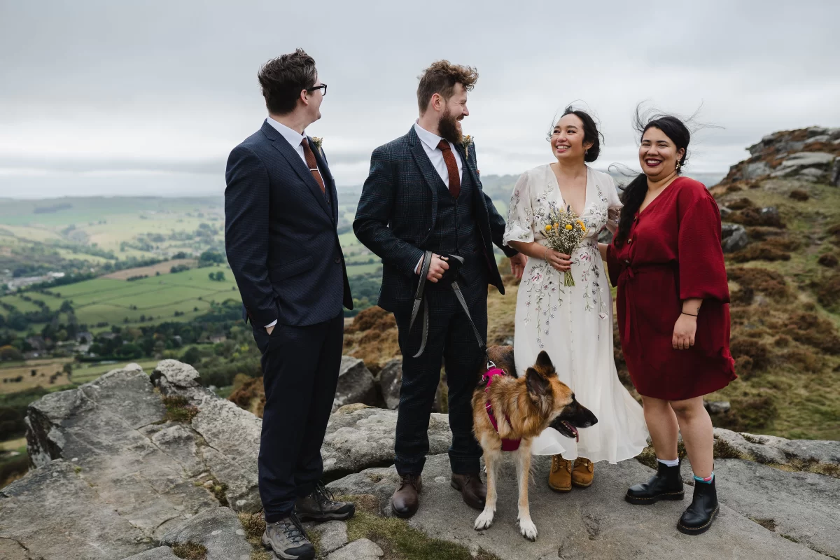 The wedding party smile together, their hair blown by the wind. Tiffin the dog is with them, a big German Shepherd.