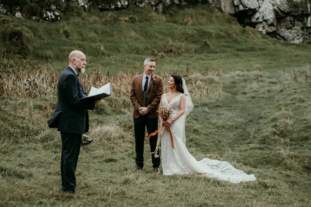 The bride and groom together in a wild location, grasses all around, with their celebrant Trevor leading the ceremony