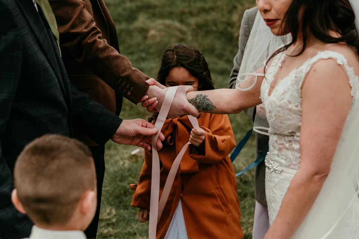 Lauren's little girl loops a pink ribbon around the bride and groom's hands