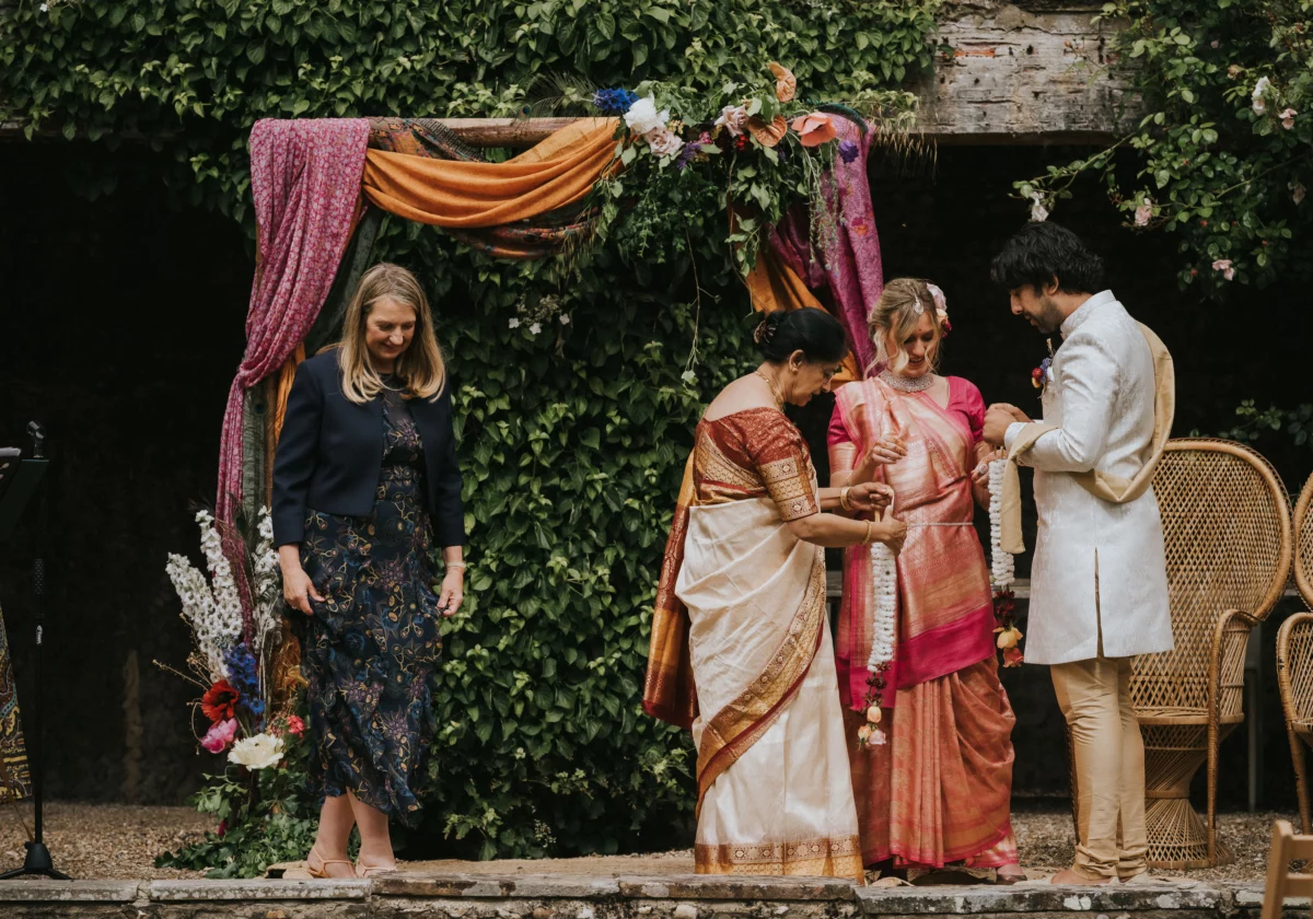 The groom's mother wears a beautiful safari and is giving the bride and groom a garland