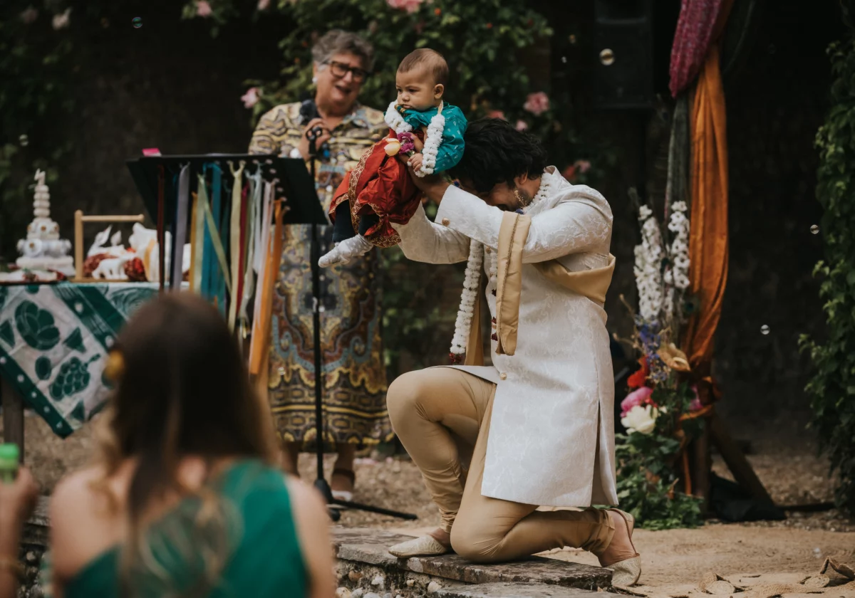 Father Amit holds baby Arti above his head while he kneels during the wedding ceremony