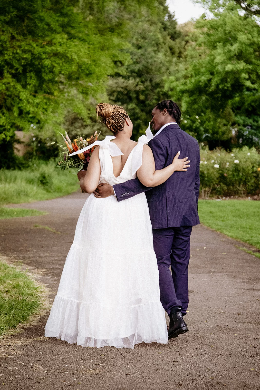 A young Black bride and groom walk outside, their arms around each other's backs
