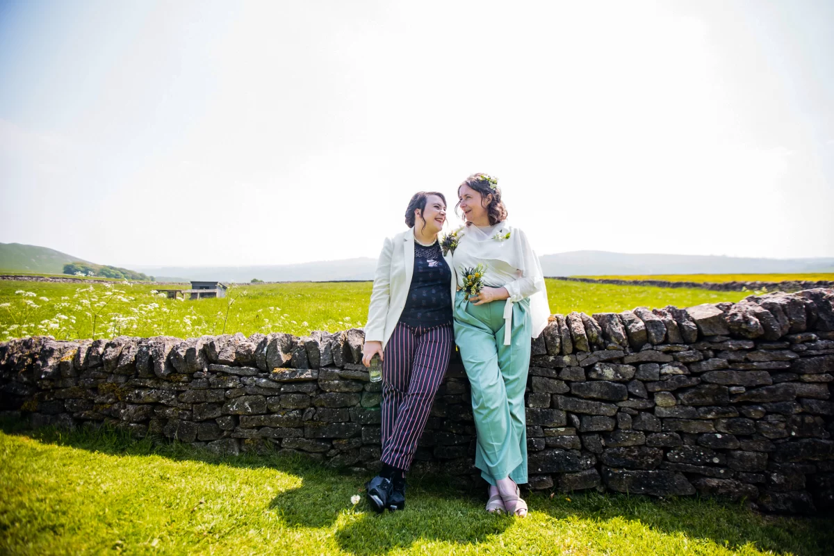 Sally and Gabby lean against a dry stone wall, relaxed and happy, surrounded by green fields as far as the eye can see