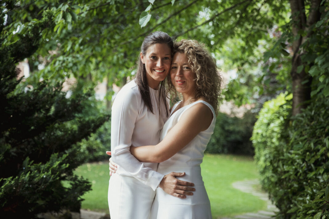 Two women dressed in white, their arms around each others' waists and heads together