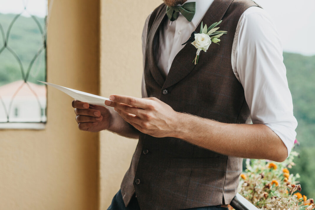 A wedding guest in a waistcoat reading from a piece of paper
