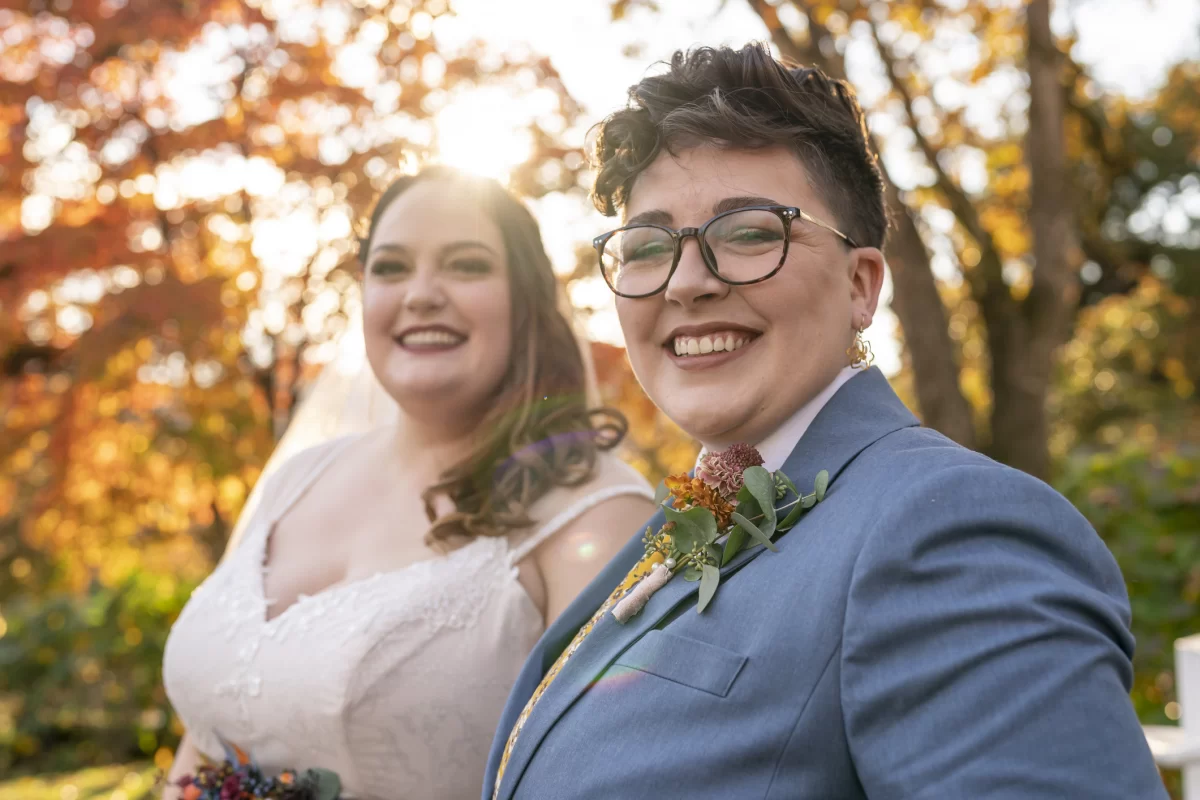 A young lesbian couple in wedding attire with autumn leaves behind them