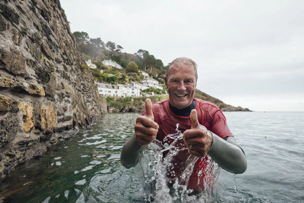 An older man, in the sea wearing a wetsuit and giving a thumbs up