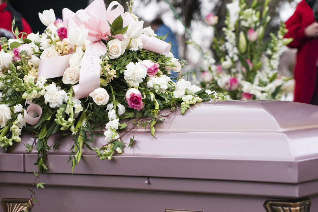 A mauve coffin with a beautiful floral arrangement laid on top