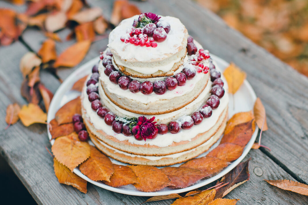 A three tier, but simple cake with cherries and icing and autumn leaves all around