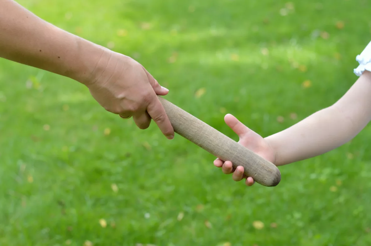 Woman's hand passing baton to a small child during a relay race