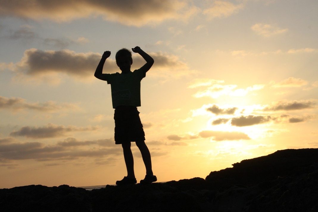 A child silhouetted against the sun, raising his arms in triumph