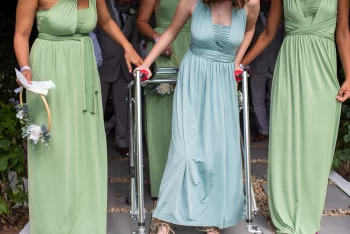 A wedding party of young women in tonal matching dresses, one is using a mobility aid.